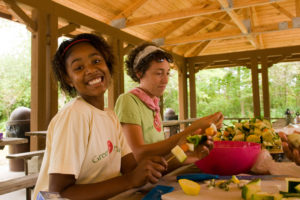 Two teenage girls making fruit kabobs with a big smile